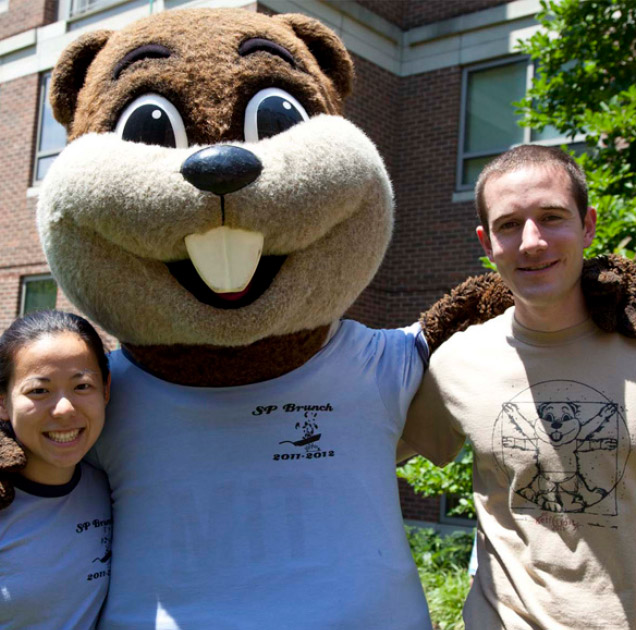 Two students pose for a selfie with MIT's mascot Tim the Beaver during a community event